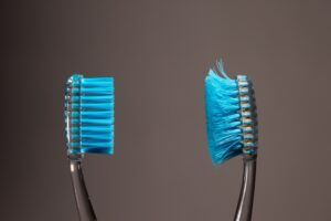 A new toothbrush with firm bristles stands next to an old, worn toothbrush